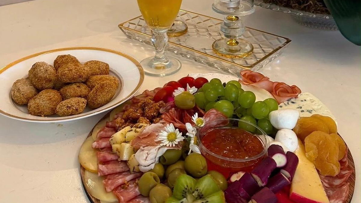 Tábua de frios com azeitonas, queijos e frutas, ao lado de um prato de salgados